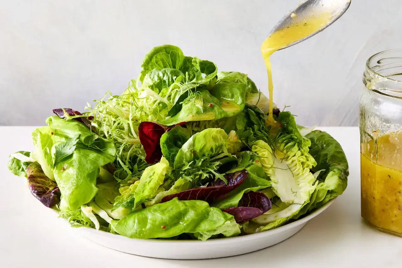 Frischer Salat wird mit selbstgemachter Salatsauce betr&auml;ufelt. Ein Glas mit der Sauce steht daneben.