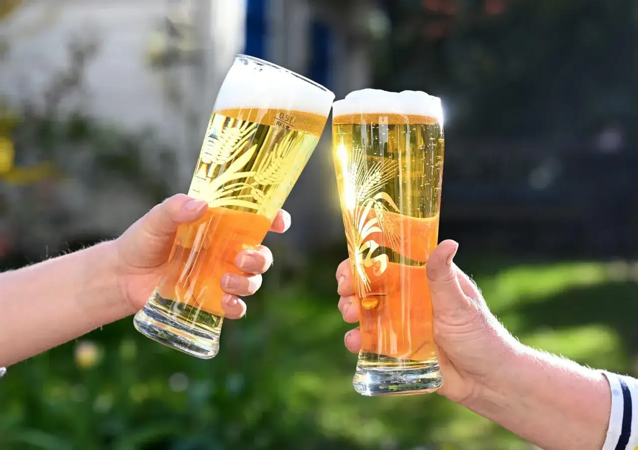Zwei H&auml;nde sto&szlig;en mit Gl&auml;sern an, die mit hellem Bier gef&uuml;llt sind. Der Unterschied zwischen Vollbier und hellem Bier wird hier bildlich dargestellt.