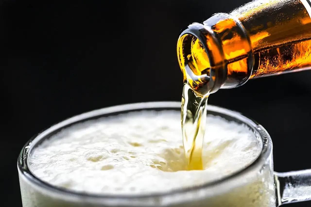 Ein goldgelbes, schäumendes Bier fließt aus einer braunen Flasche in ein Glas. Perfekt für alle, die alkoholfreies Bier selber brauen möchten.