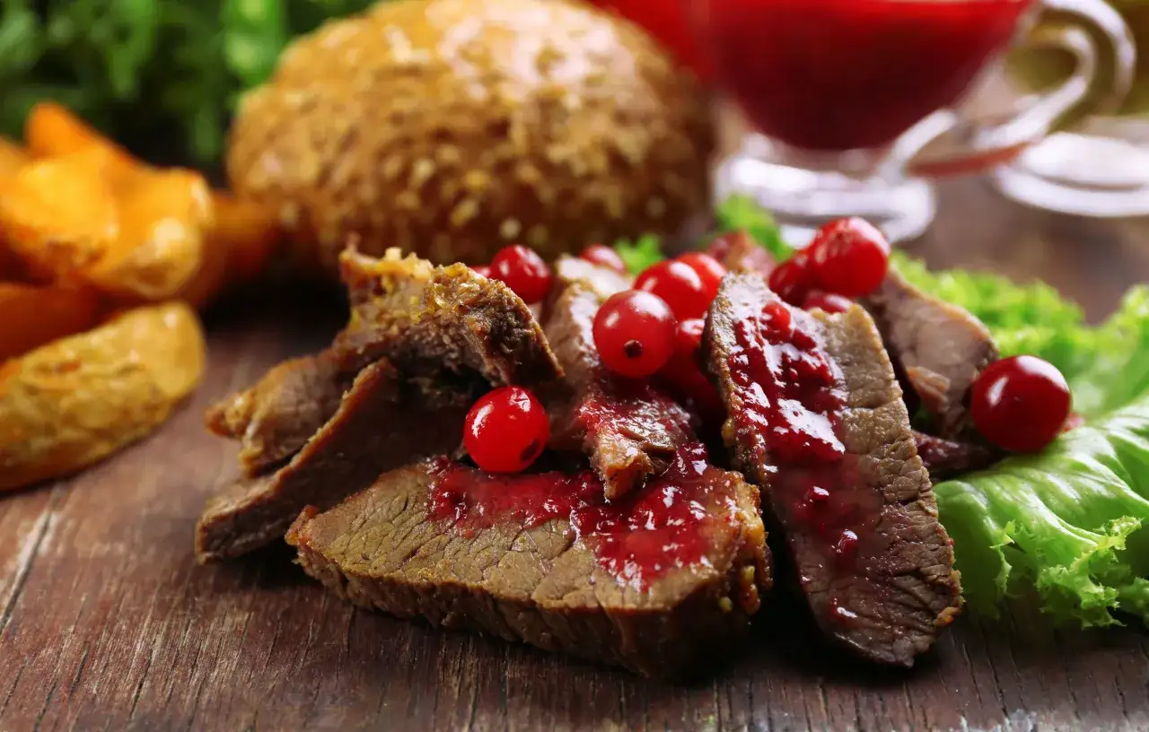Schmackhafter Hirschbraten geschmort, serviert mit roten Beeren und Kartoffelspalten. Ein k&ouml;stliches Rezept f&uuml;r Genie&szlig;er.