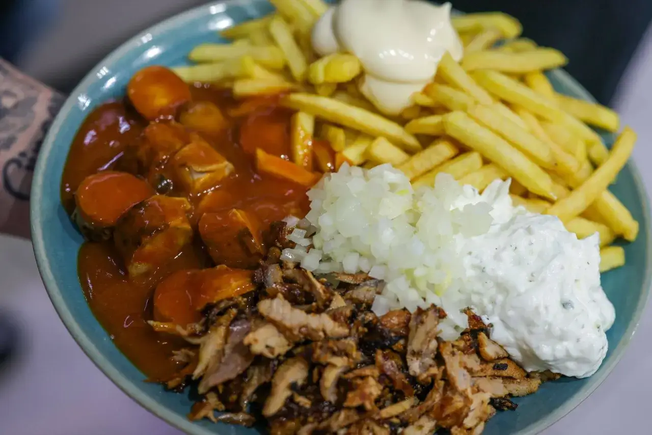 Teller mit Currywurst, Pommes, D&ouml;nerfleisch, Zwiebeln und Joghurt-Dip. Ein Klassiker f&uuml;r den schnellen Hunger.