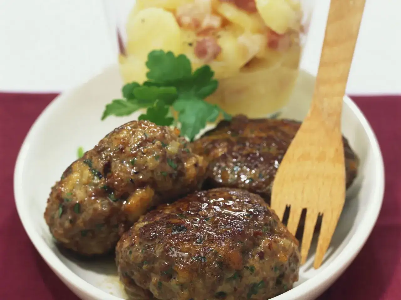 Saftige Frikadellen, perfekt für ein schnelles Frikadellen Rezept, serviert mit Kartoffelsalat und einem Holzlöffel.