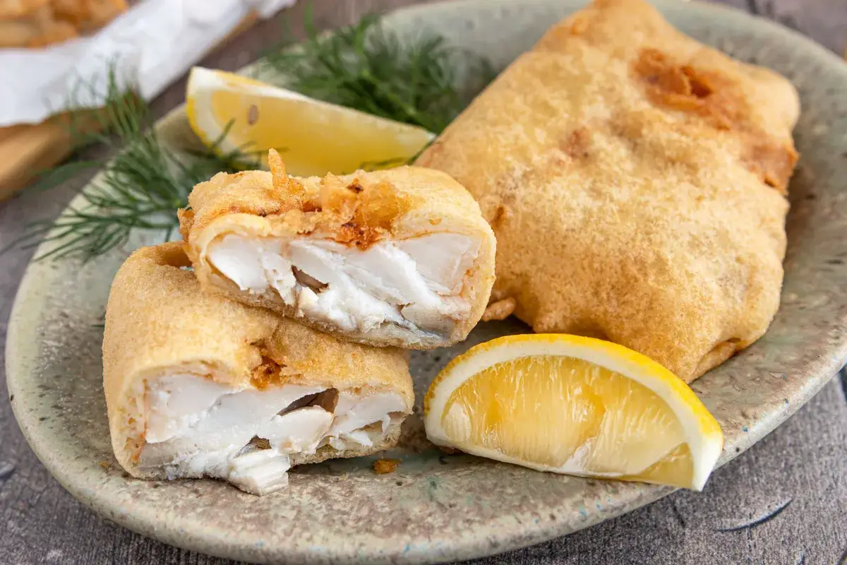 Knuspriges Fischfilet in Treber Panade, serviert mit Zitrone und Dill.