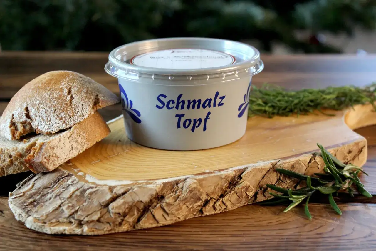 Schmalztopf mit Brot und Rosmarin. K&ouml;stliche Schmalzrezepte f&uuml;r Brotaufstriche, die auf rustikalem Holz serviert werden.