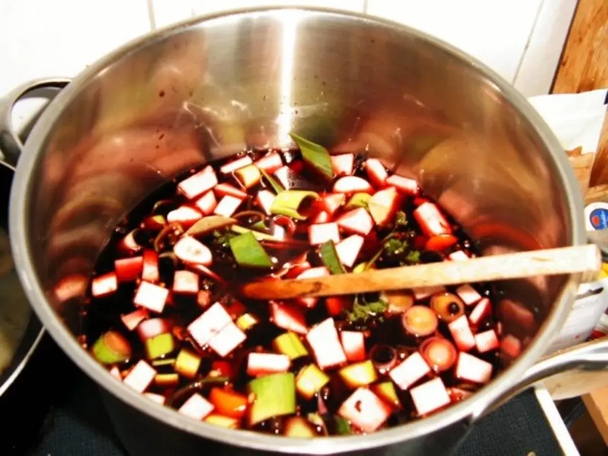 Sauerbraten einlegen in Rotwein mit Gem&uuml;se. Ein Holzl&ouml;ffel liegt in der Marinade.