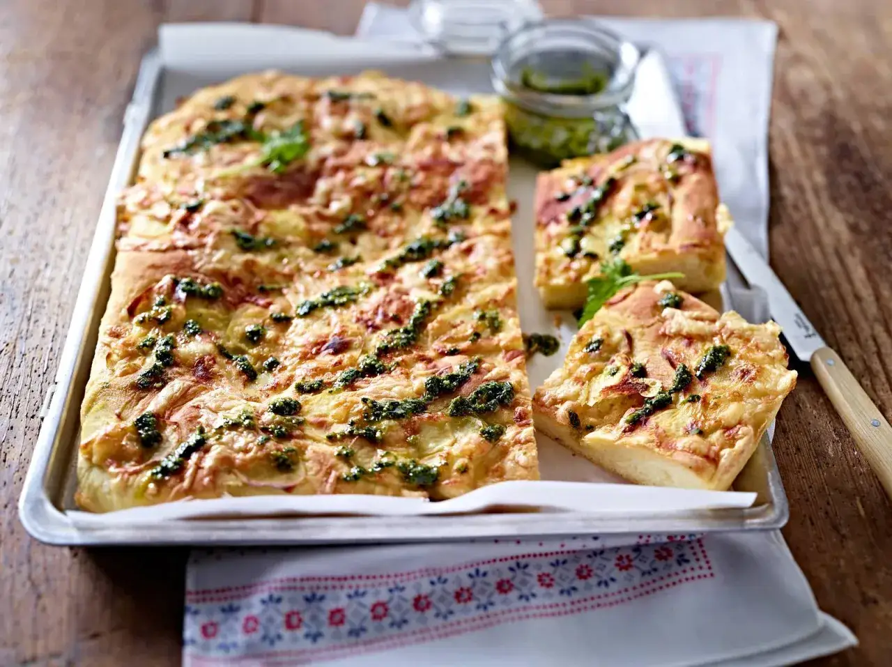Ein rustikaler Kartoffelkuchen nach altem Rezept, belegt mit K&auml;se und Kr&auml;utern, serviert auf einem Blech.