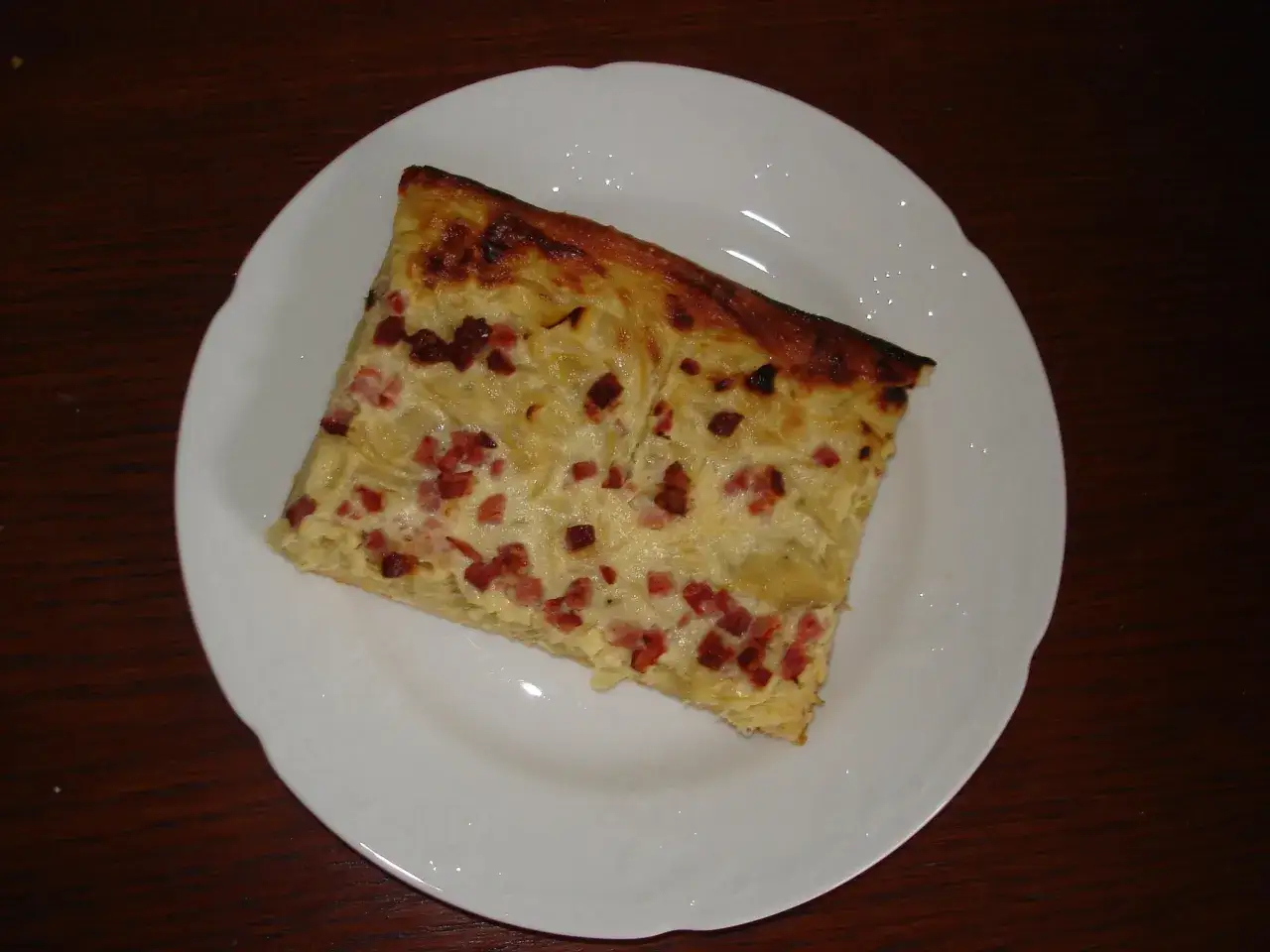 Ein Stück Zwiebelkuchen mit Speck auf einem weißen Teller. Dieses Gericht ist ein Klassiker, der nach einem originalen Rezept zubereitet wurde.
