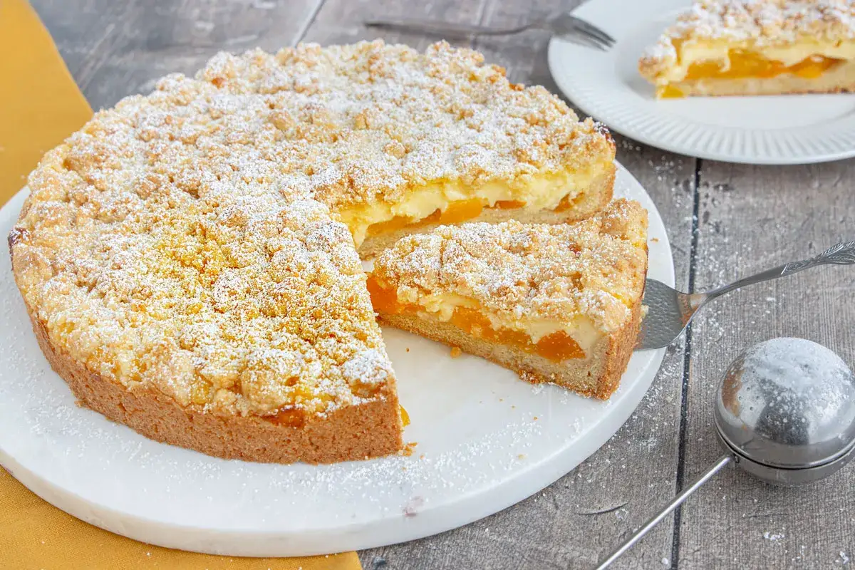 Ein saftiger aprikosenkuchen mit pudding und Streuseln, best&auml;ubt mit Puderzucker. Ein St&uuml;ck wird gerade serviert.