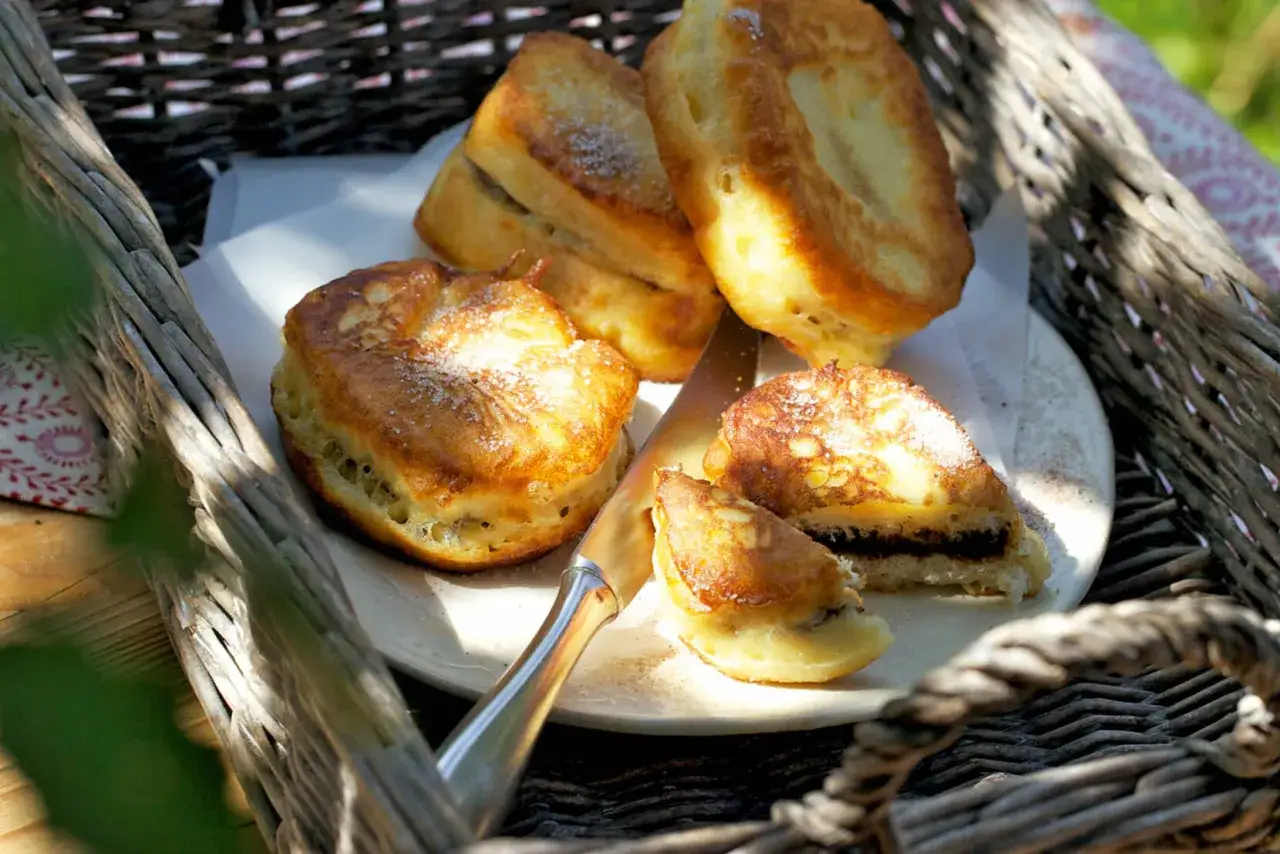 Goldbraune Zwetschgenbavesen, mit Zucker bestreut, warten auf das Zwetschgenbavesen Rezept. Ein Messer liegt daneben.