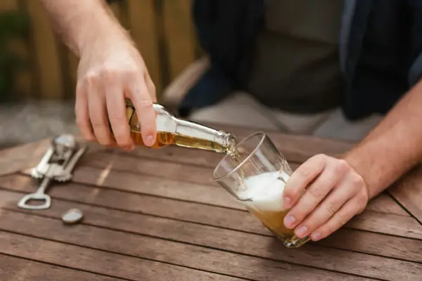 Mann schenkt Bier ein. Vielleicht für ein 20-Liter-Bier-Rezept? Ein Kronkorken und ein Flaschenöffner liegen bereit.